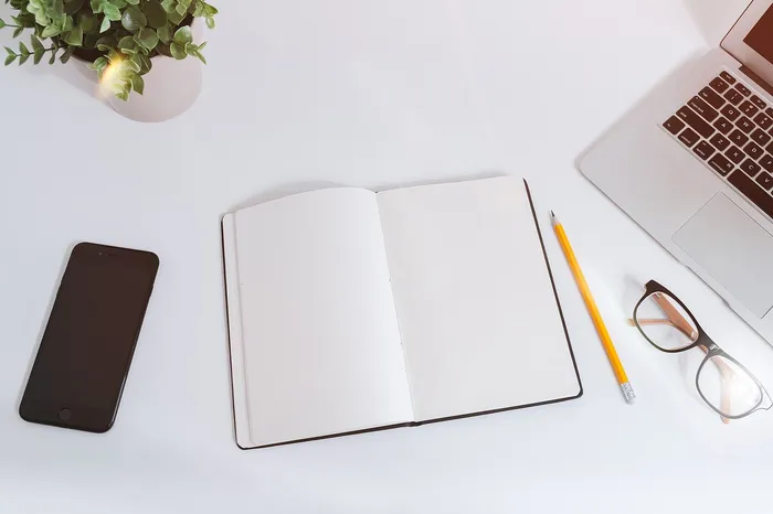 Mesa de trabajo blanca con un portátil, un móvil y una libreta abierta